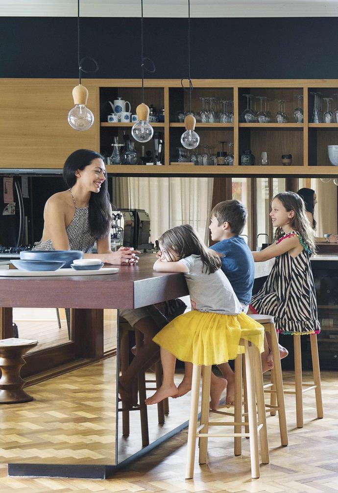 **Portrait** Veronique and her children use the kitchen island as a multi-purpose space. The mirrored base of the island reflects natural light and makes the space feel even bigger than it is. A trio of pendant lights add a warm touch, echoing the timber stools and cabinetry in the kitchen. "The kids eat and do homework at the bench. We also entertain quite a bit… it's easy to entertain in," says Veronique.