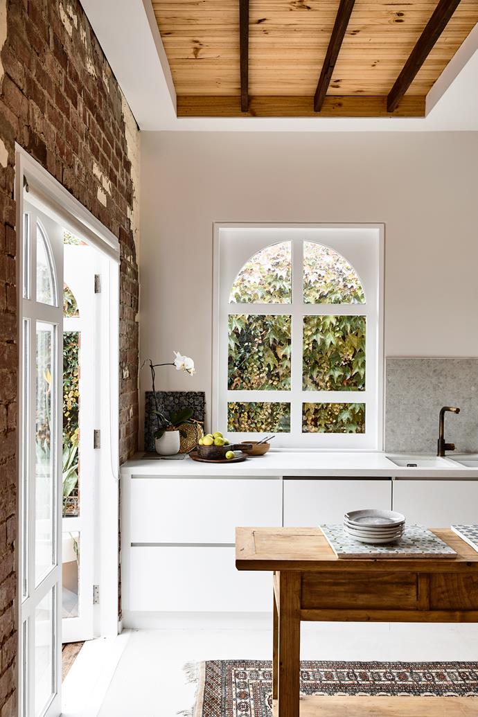 The original Art-Deco features of this home shine through in the kitchen, from the exposed beams to the textural brick wall. Meanwhile, an arch window provides the perfect backdrop for days spent baking and an antique rug tucked under the timber island keeps it cosy. 

*Photographer: Derek Swalwell*