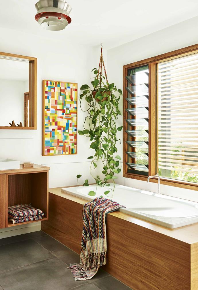 The hard lines of the bathroom joinery, designed by Sarah and constructed by Geoff Rodgers Cabinets, are softened with the free form of the impressive hanging philodendron. Plants are important to the green-thumbed family. "I've always grown up with plants and flowers," says Sarah. "The trick with indoor plants is to not over-water!" The vibrant tones in the artwork by Georgia Gray are held in a frame that matches the blackbutt vanity and bath surround. Bath sheets, [Sage and Clare](https://sageandclare.com/|target="_blank"|rel="nofollow"). <br><br>**Tip**: Humidity-loving plants instantly change the feel of your bathroom, without the cost of a makeover.