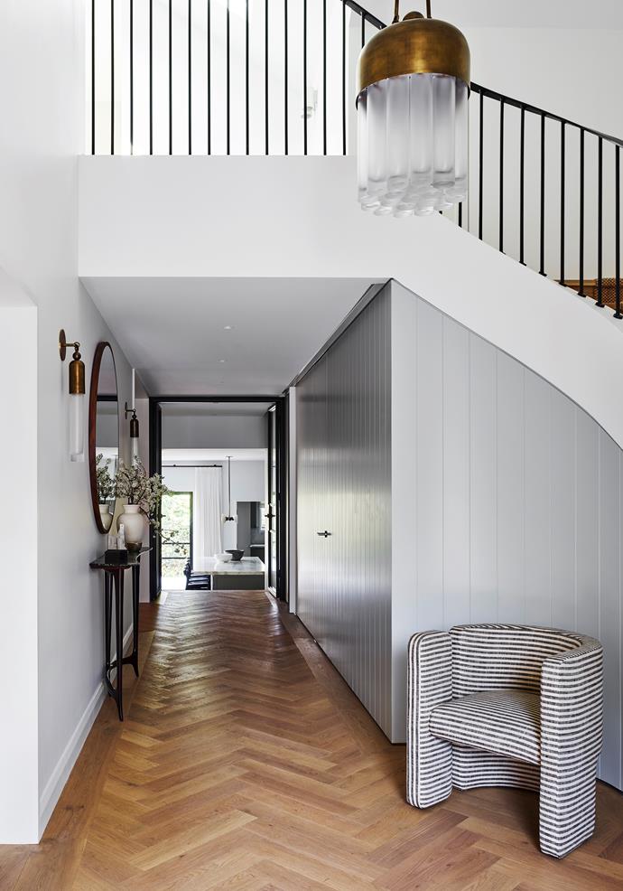 This [home on Sydney's north shore](https://www.homestolove.com.au/sydney-home-by-arent-and-pyke-19550|target="_blank") has been transformed by interior design studio Arent&Pyke. Above the sculptural, redesigned staircase hangs an Apparatus 'Tassel' pendant in aged brass, while a Kelly Wearstler 'Fairfax' chair in ivory and charcoal stripes complements the linear looks of the hallway.
