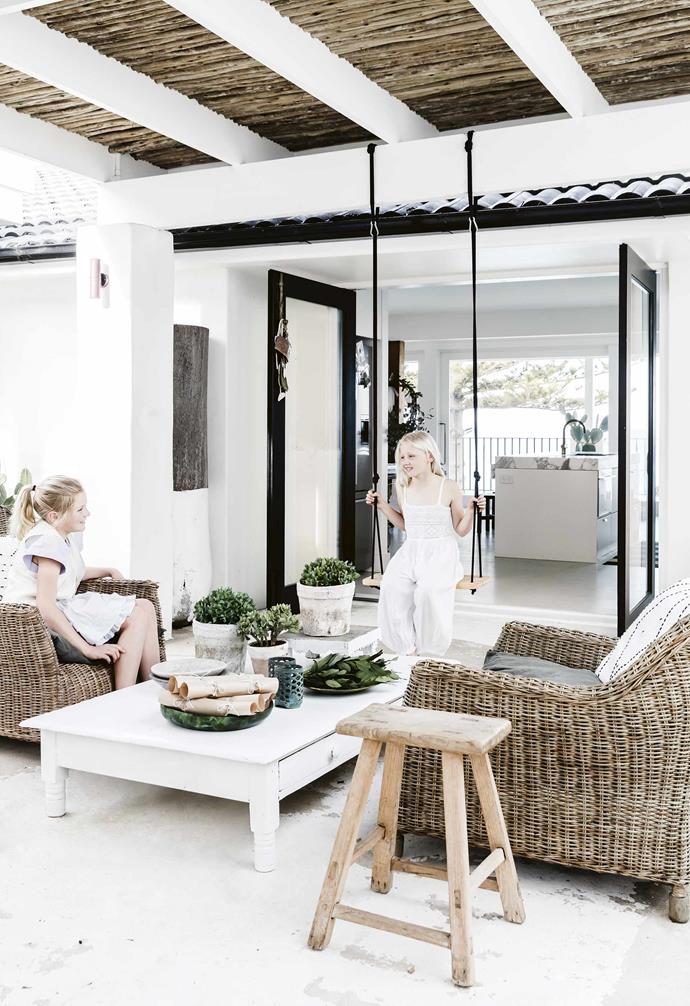 This Mediterranean-inspired all-white holiday home features an incredible outdoor living area complete with a swing for the children to play on. The outdoor zone is connected to the indoor kitchen space with black timber-framed glass doors.
