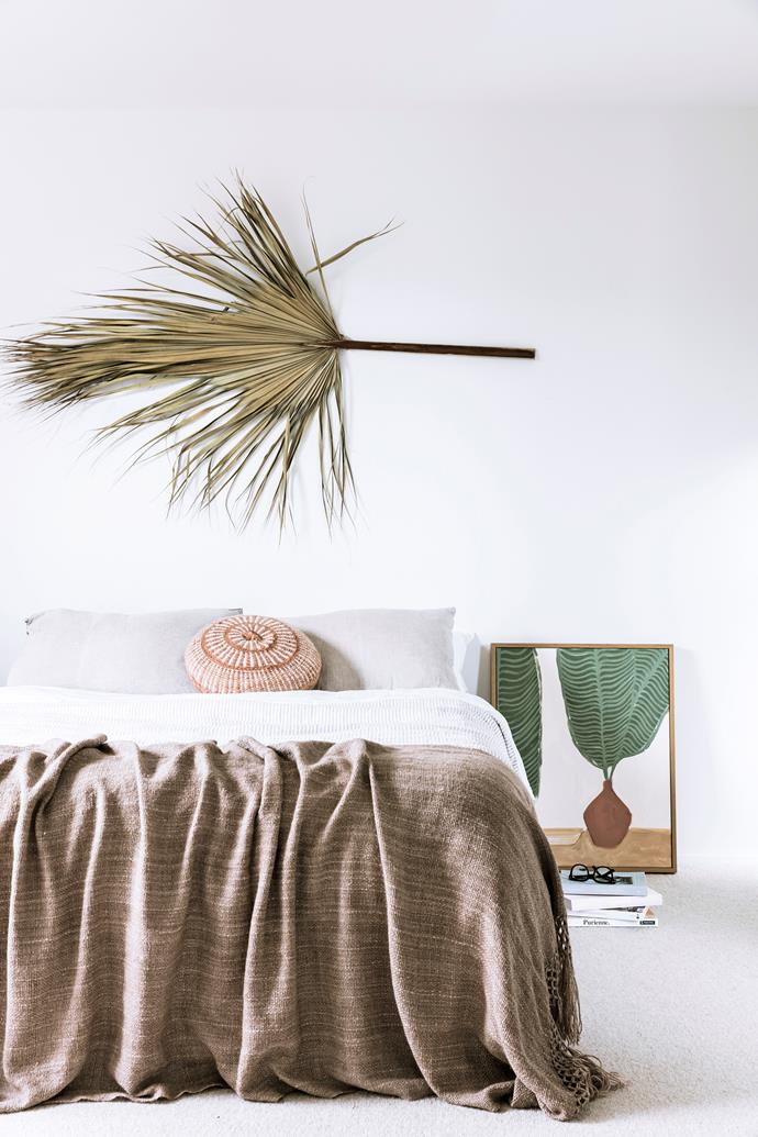 In a nod to the home's coastal location, the couple's bedroom features textural woven bedding, a tropical-themed artwork and a dried palm frond-turned-wall feature.
