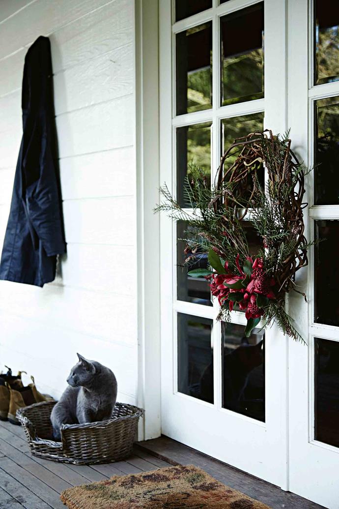 Yogi the Russian Blue cat sits by the back door of a house on a [miniature donkey farm in West Gippsland, VIC](https://www.homestolove.com.au/celebrating-christmas-on-a-miniature-donkey-farm-12168|target="_blank"). A wreath of fresh foliage brings Christmas cheer to the exterior of the home, while a string of festive bunting welcomes visitors to the property at the front gate.
