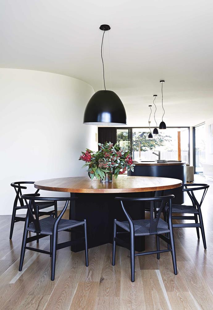 Black chairs and large pendant lights provide a striking contrast to the light wood floors in the dining zone in this [contemporary beach house retreat](https://www.homestolove.com.au/how-to-create-a-contemporary-beach-house-retreat-17299|target="_blank"). The black dining chairs and dark base of the timber-topped dining table echo the design of the statement kitchen island.