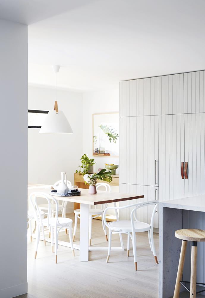 Set to the side of a generous open-plan kitchen and living space, the dining room is placed next to a generous window that allows ample natural light to illuminate the heart of this [coastal holiday home](https://www.homestolove.com.au/coastal-holiday-home-19311|target="_blank"). White Thonet dining chairs are paired with a timber dining table and statement white sculptural pendant light. 