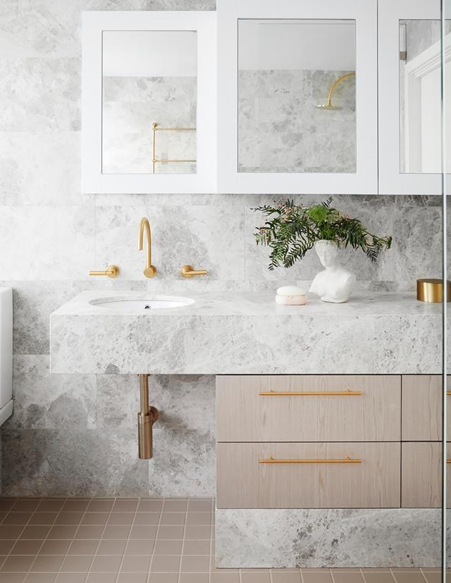 Beautifully bright and breezy, [this coastal abode's](https://www.homestolove.com.au/white-beachfront-home-with-coastal-style-21079|target="_blank") bathroom features glam finishes and fittings. Elegant Casa honed-limestone wall tiles are offset by gold tapware and an engineered-timber vanity front.