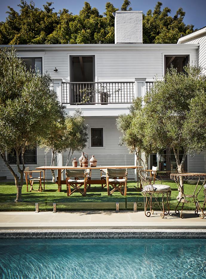 Verdant lawns and a swimming pool in the backyard add to the property's family-friendly appeal. The vintage iron table and chairs are from JF Chen and the teak dining table is from Leif. Atop it are cane wine bottles from Rose Bowl Flea Market.