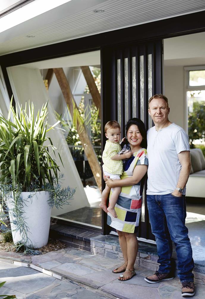 "The original '60s design was very bright and open," explains Jung, adding that a renovation in the 1970s had changed all that. "There were [turquoise wallpaper](https://www.homestolove.com.au/statement-wallpaper-designs-5696|target="_blank") and moons and stars painted on the cupboard doors. The original stove was still here but the oven had rusted out because of leaks. There was wood-veneer panelling on the A-frame walls that was peeling. Even the A-frame beams were mission brown. The first time it rained, we were running around placing buckets all over the house!"<br><br>**Portrait** Owners Jung and Bart with their son Arki.