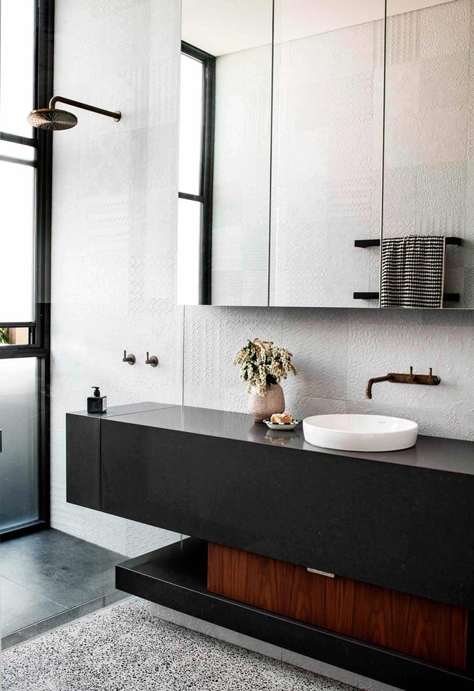 White textured tiles create a dramatic backdrop in the bathroom of this [contemporary home in Booker Bay](https://www.homestolove.com.au/modern-house-booker-bay-20437|target="_blank"). The statement black and timber vanity adds a striking highlight to the space and beautifully complements the terrazzo flooring.