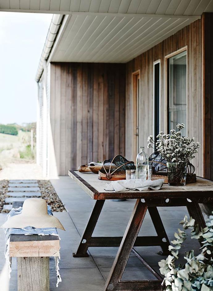 The outdoor dining area on the verandah of this [designer's home in Freshwater Creek, Victoria](https://www.homestolove.com.au/designer-dream-home-in-freshwater-creek-victoria-13657|target="_blank") features a minimal but stylish dining table and a homemade bench, with a cosy through thrown over it for comfort, and simple field flowers to make every meal feel like a special occasion.
