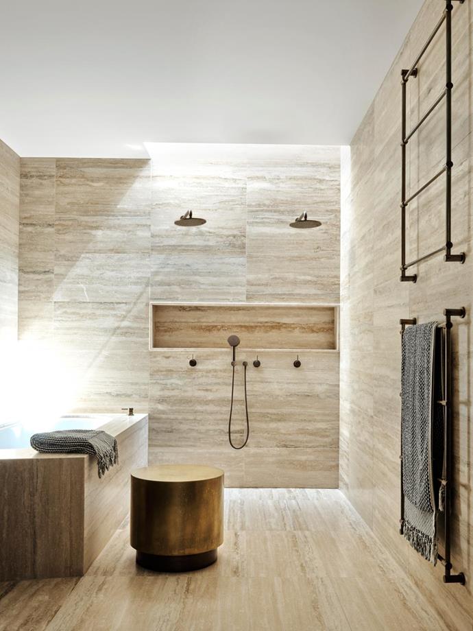 Silver travertine tiles emit a warm glow in the bathroom which features a stone basin and shower niche designed by Flack Studio, plus aged-brass Astra Walker tapware and towel ladders and a Baxter 'Loren' table from Criteria.