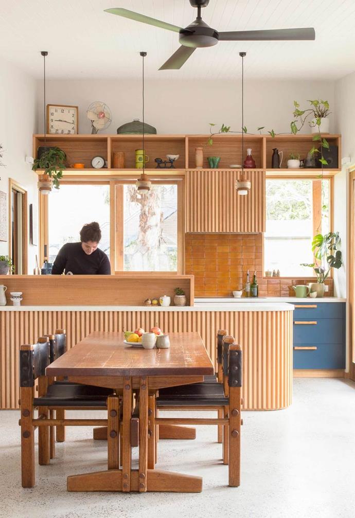 A range of different textures sing in this [timber kitchen space](https://www.homestolove.com.au/eco-friendly-melbourne-bungalow-17260|target="_blank") with glossy amber subway tiles forming the splashback. Blue cabinetry features timber handles that echo the rest of the space and white benchtops echo the light flooring. The soft curve of the kitchen island adds an organic shape, and is clad in recycled messmate timber battens. 