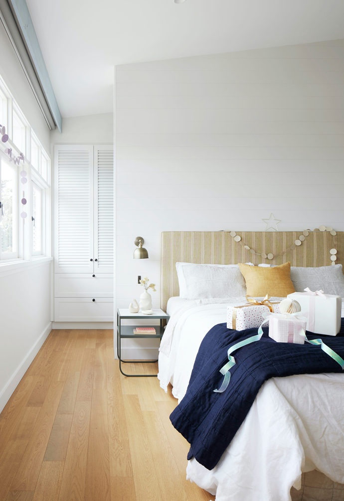 The decorating scheme in the master bedroom nods to Rhiannon's cool, [coastal style](https://www.homestolove.com.au/8-ways-to-get-coastal-style-12277|target="_blank") with subtle stripes, a shutter-front robe and white wall panels. The bed and cushions are from The Boathouse Home, the bedside is from Great Dane and the couple found the wall sconce while in London. Garlands from Pulp Creative Paper, ceramics from Makers' Mrkt and presents with paper and ribbon from Vandoros.