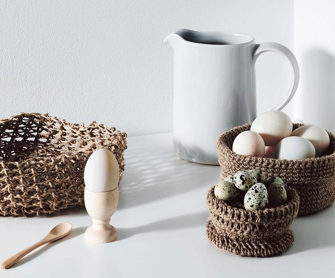 Crocheted string baskets filled with eggs on a white table next to a milk jug