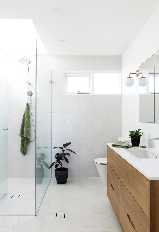 Shower tile designs continued throughout the entire space results in a sleek, cohesive look, like in [this mid-century modern-style bathroom](https://www.homestolove.com.au/mid-century-modern-coastal-home-freshwater-22223|target="_blank"). The hexagonal shape adds interest and wraps from the floor up the wall where a skylight directly above the shower floods the space with natural light.