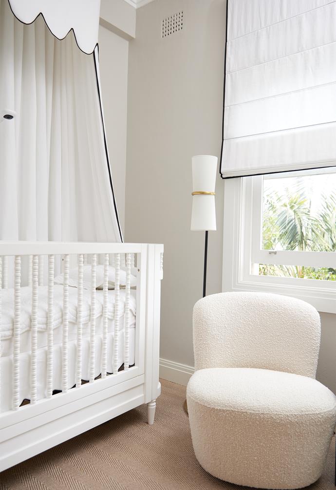 A cosy [bouclé chair](https://www.homestolove.com.au/boucle-furniture-21234|target="_blank") sits beside an antique-style cot and its charming scalloped canopy.