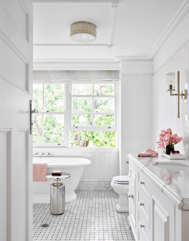 An all-white bathroom is punctuated with pink accessories in [this beautifully restored federation home](https://www.homestolove.com.au/glamorously-restored-federation-home-22400|target="_blank"). The Kaldewei 'Vaio' bath sits atop detailed marble mosaics, while statement brass wall sconces and a shiny side table offer stylish functionality.