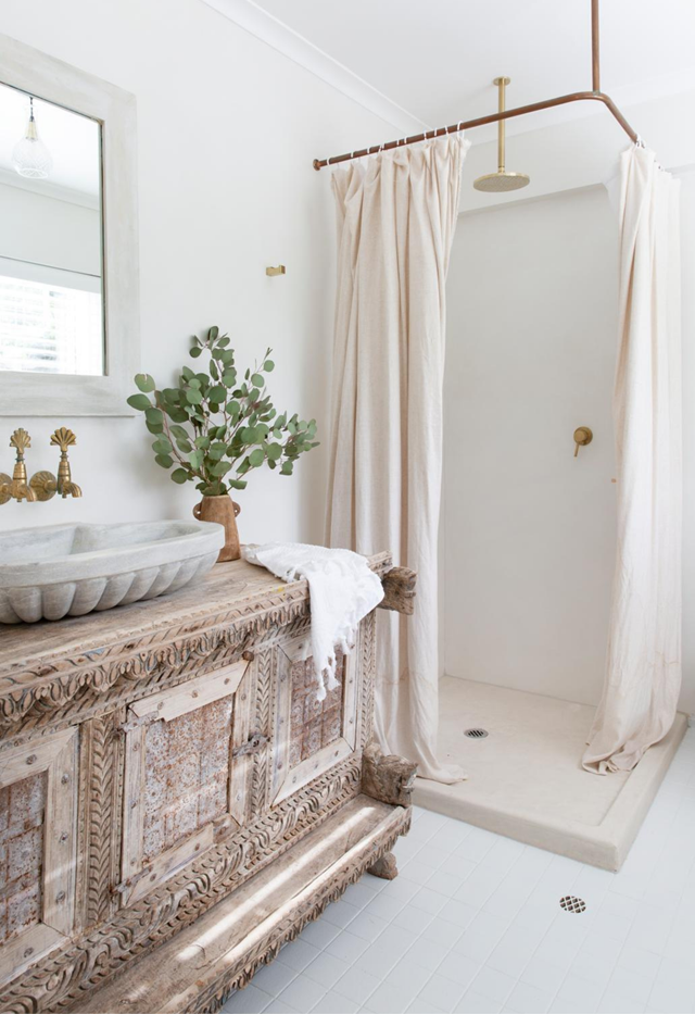 **Rustic luxury**<br>
Hotel-like luxury is offset with a rustic aesthetic in [this simple, textural space](https://www.homestolove.com.au/white-on-white-coastal-home-noosa-22415|target="_blank") via the elaborate tapware, marble fluted basin and vintage trunk-turned-vanity. The plantation-shuttered windows bring in lots of natural light, while a charming curtain covers the shower.