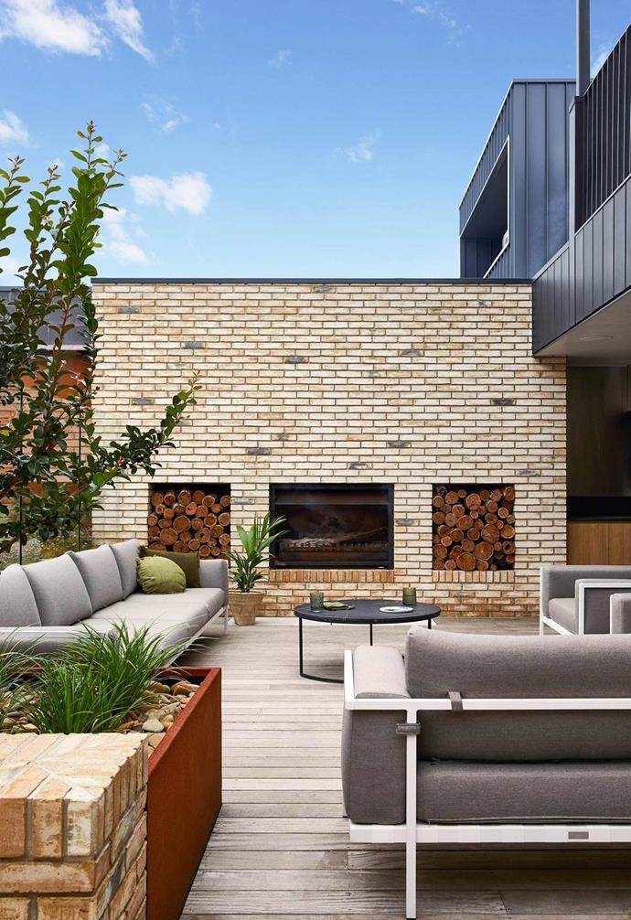 In this outdoor living space at a [contemporary family home](https://www.homestolove.com.au/contemporary-family-house-torquay-22236|target="_blank") in Torquay, a wall of Danish-blend bricks creates privacy as well as a cosy hub for an outdoor fireplace. Niches in the wall act as the perfect storage for firewood and kindling. As trees surrounding the deck mature, they will increase shade cover, creating a space that is enjoyable in both winter and summer.