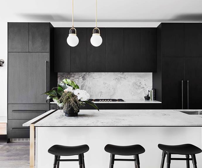 The kitchen in the Albert Park home features dark cabinetry and light marbled stone on the island bench and splashback.