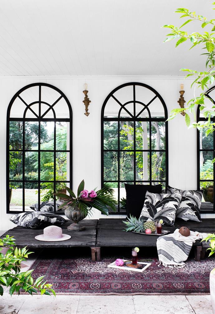 The ground level verandah provides a spot for breezy lounging, framed by a series of arched mirrors from One World Collection and vintage wall sconces from Lunatiques. The daybed is made from reclaimed timber pallets with cushions from Great Outdoor Cushions and a vintage Persian rug.