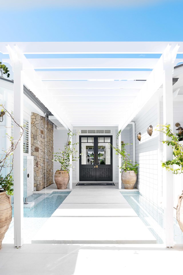 Located in Noosa, [this Hamptons-inspired home](https://www.homestolove.com.au/hamptons-christmas-home-23131|target="_blank") is as pretty as a picture, with all the extras of a tropical resort. While water is the central feature at the entrance, terracotta urns filled with bougainvillea evoke a tropical vibe. The doors, painted in [Benjamin Moore](https://www.homestolove.com.au/where-to-buy-benjamin-moore-paint-in-australia-23214|target="_blank") Hale Navy, provides a taste of the coastal palette beyond.