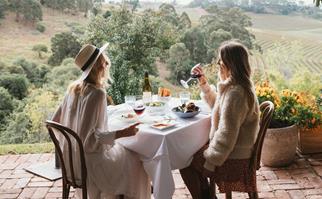 Two women dining outdoors in the Hunter Valley on a deck overlooking a vineyard