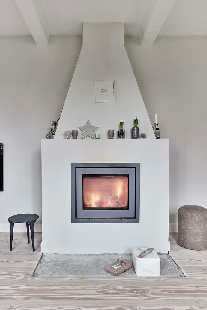 The simple fireplace is the centrepiece of the living room. On the floor in front is an Italian black lava stone, to protect against sparks. On the mantelpiece are hyacinths set in glass vases.