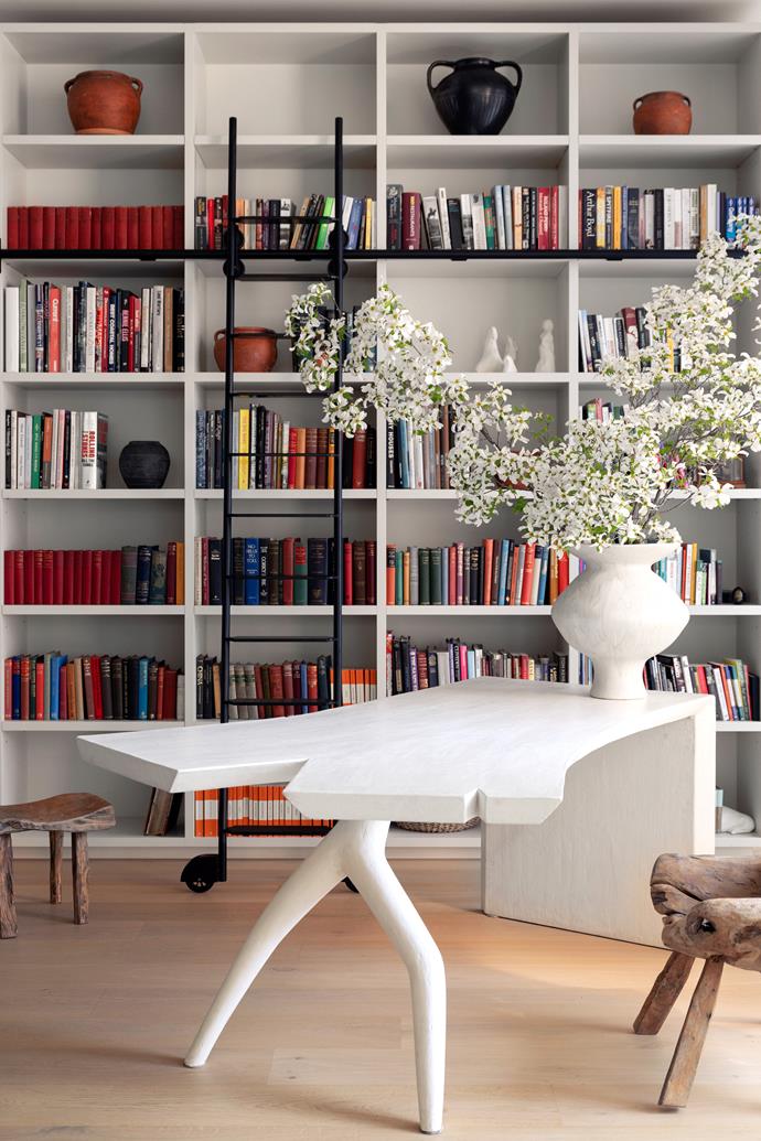In the library with custom shelving by Silhouette Kitchens, a chair from Watertiger sits at the plaster table with white vase, both client's own.
