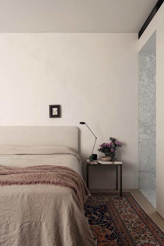 The main bedroom, with its subdued palette, is a serene sanctuary. The client's own Indian engraving hangs above the custom bedhead. Lumina 'Daphine' table lamp by Tommaso Cimini from Enlightened Living on a custom-made bedside table with Calacatta Viola top.
