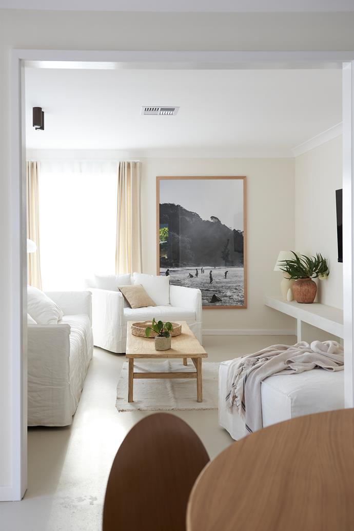 The lounge room is coastal chic, with white linen and pale timbers. The couches are from Lounge Lovers, and the framed print is by Kara Rosenlund.