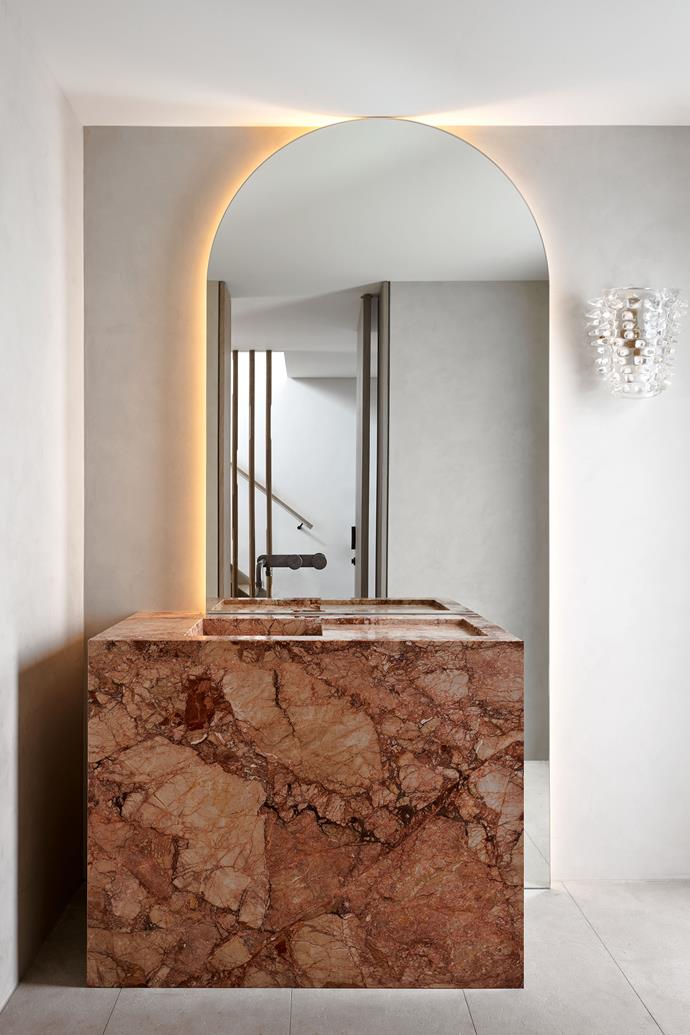 A glamorous powder room on the entry level has a vanity in Tiberio honed marble from Artedomus. Flooring in Garonne limestone from Eco Outdoor. Antique wall sconce from Tamsin Johnson.
