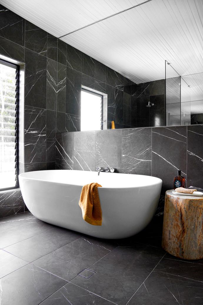 **BATHROOM** Floor-to-ceiling 'Pietra Grey' marble tiles from Phil's Tile Warehouse set the scene for a freestanding bath, bought online, that's paired with Reece tapware and positioned to take in rainforest views.  A log stool, made by Max, provides the perfect perch for soaps, while Adairs towels add a touch of colour to the monochrome scheme.
