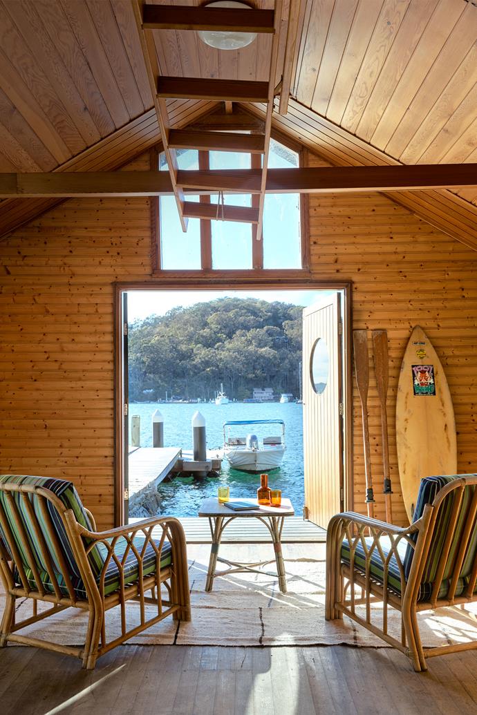 The boatshed is bathed in morning sunlight, making it a magical spot for breakfast or lunch by the water. Existing chairs were reupholstered in a vintage fabric. Vintage Turkish hemp rug from Garden Life. The ladder hanging above leads up to the mezzanine sleeping quarters.