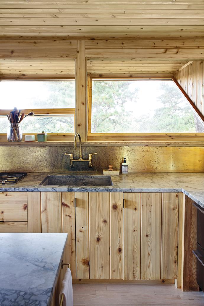 Some kitchens have amazing outlooks; this one has incredible geometric windows where the bottom part opens up but the top is fixed. At the sink is an aged brass splashback.