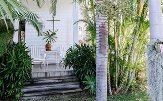 Exterior of a renovated, white beach cottage surrounded by palm trees and tropical garden plants