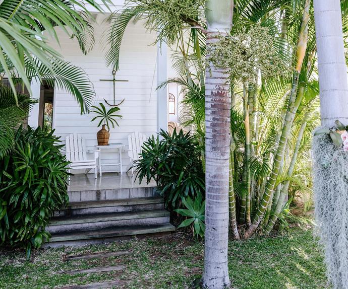 Exterior of a renovated, white beach cottage surrounded by palm trees and tropical garden plants