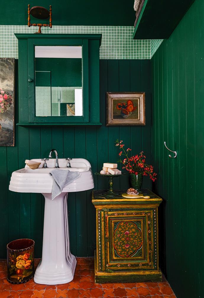 Deep, dark green clashes delighfully with red and terracotta/mustard tones in the bathroom of this pink [lakeside cottage on the Sunshine Coast.](https://www.homestolove.com.au/pink-lakeside-cottage-sunshine-coast-23361|target="_blank")  The original art deco sink lifts the room whilst the decorated chest found, which was found in an English antiques store, adds an element of luxury.