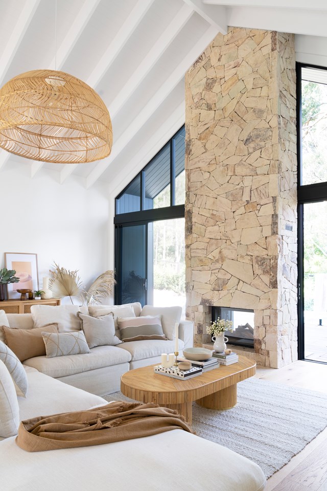 Soaring ceilings call for dramatic effect in [this Gold Coast hinterland home](https://www.homestolove.com.au/gold-coast-hinterland-modern-log-cabin-23362|target="_blank"), with a 5.5m  stacked stone fireplace set among a wall of glazing. The wood-burning fireplace is glass on both sides, making the bush visible from the inside when it's not lit, while the flames can be enjoyed from outside on the deck when alight.