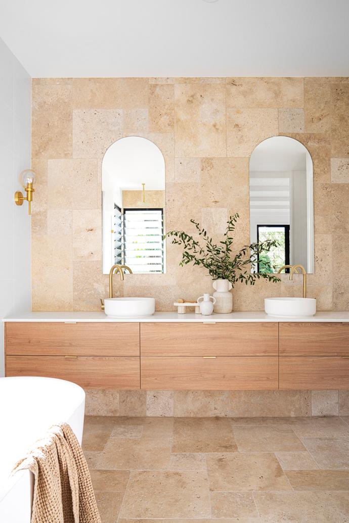 **ENSUITE** "We wanted to create an ensuite that felt like a total escape," says Ema of the luxe space. Floor-to-ceiling travertine tiles from [National Tiles](https://www.nationaltiles.com.au/|target="_blank"|rel="nofollow") formed the foundation. To complement the backdrop, a custom vanity by Cuisine Kitchens in Polytec woodmatt MDF in Tasmanian Oak features ABI Interiors brass tapware and Fienza basins. A vase from Magnolia Lane filled with foliage adds to the organic look. Mirrors by [Millennium Glass](https://www.millenniumglass.com.au/|target="_blank"|rel="nofollow") reflect views, while Beacon Lighting wall lights add a further touch of brass.