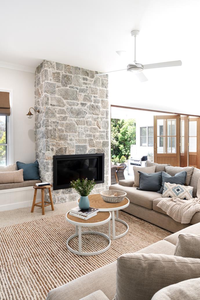 **LIVING AREA** While the kitchen has a coastal feel, the living area exudes country cosiness, complete with a Mr Stoves fireplace enveloped in a [stacked limestone wall](https://www.homestolove.com.au/stone-feature-walls-21461|target="_blank") installed by Stone Nation. "In winter, we have a fire every night and most mornings," says Kristy. Custom bifold timber doors by Front Porch Properties help connect the space to the alfresco entertaining area, while a window seat is a quiet spot for reading.