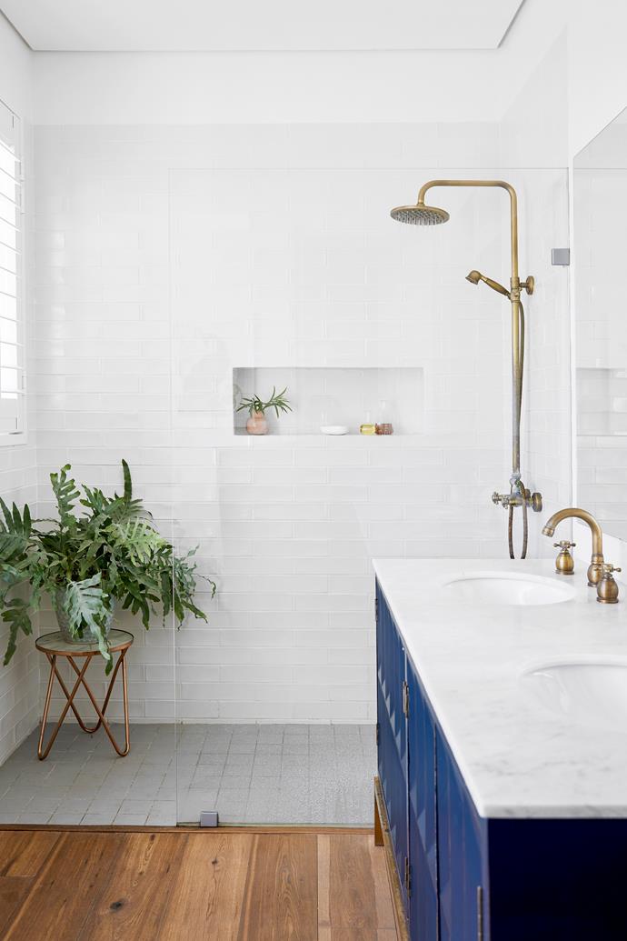 The gorgeous bathroom of this stunning sun-drenched [Cape Town home](https://www.homestolove.com.au/self-sufficient-cape-town-home-and-garden-23449|target="_blank") demarcates different 'zones' by a change in flooring. Deep blue cabinetry come stogether with brass tapware and marble for a look that is sophisticated and timeless.