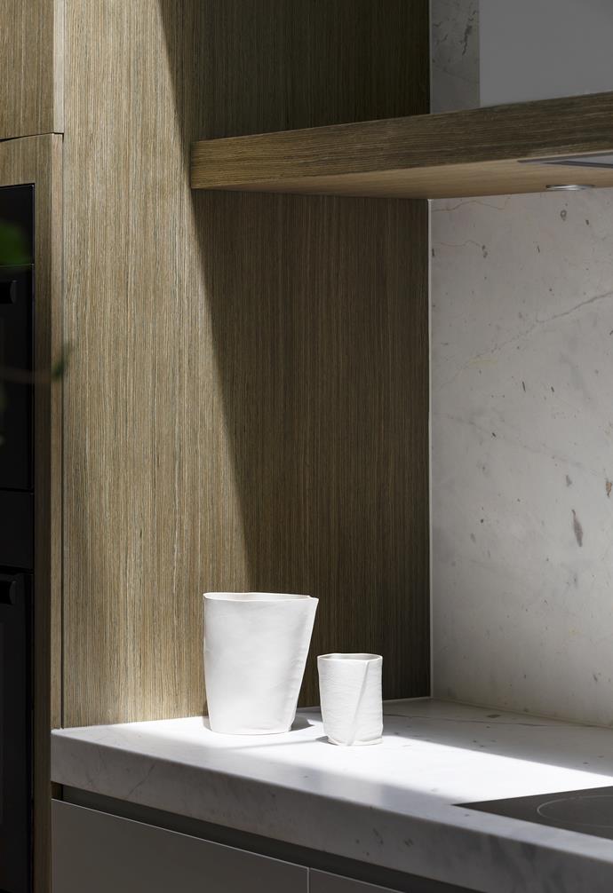 In a corner of the kitchen, dark timber veneer lends a contrast to the Elba marble splashback in pattern and palette, with the expanse of stone neatly broken up by the floating shelf. Ceramics by Criteria Collection.