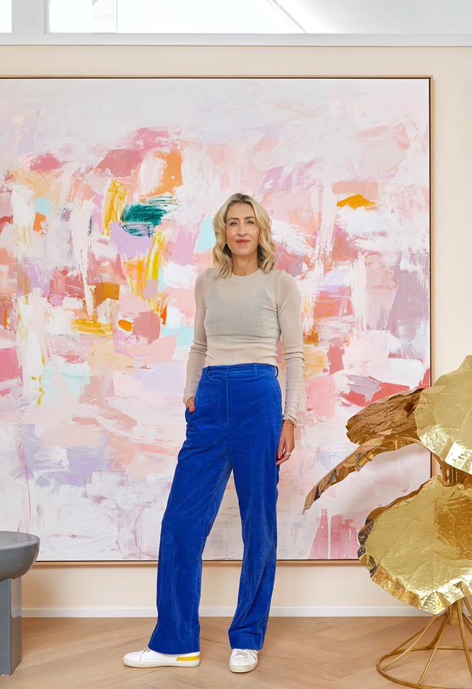 Kirsten stands in front of her Let's Go Dancing artwork, which helped inform the home's colour palette. Beside her, an extravagant golden Domo floor lamp commands attention but doesn't overpower the painting.