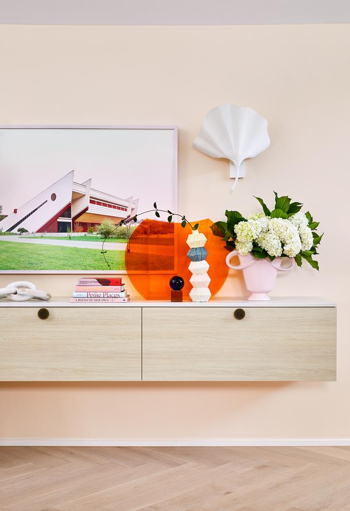 A slab of Caesarstone Fresh Concrete atop wall-mounted drawers by Total Cabinetry Solutions creates a neat display area in the living room. Above the shelf, a print by Dave Kulesza mirrors the clean-lined vibe of the home. The mementos include a vintage orange Perspex vase and a concertina vase by Kirsten Perry.
