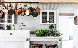 a marble kitchen with brass pots hanging above and fresh cut herbs on the benchtop