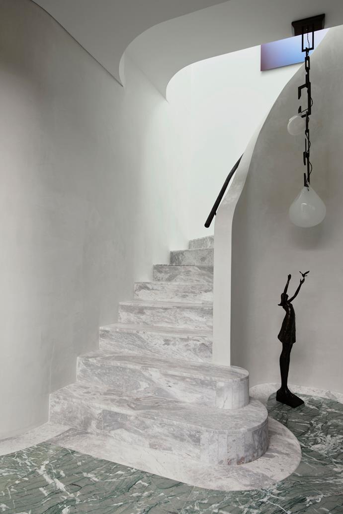 At the home's entrance a curved Elba marble staircase is offset by a Nepenthes light by Christopher Boots and Bronze Statue Aurora IV by Tom Corbin. The floor is a solid slab of Verde Antigua marble.