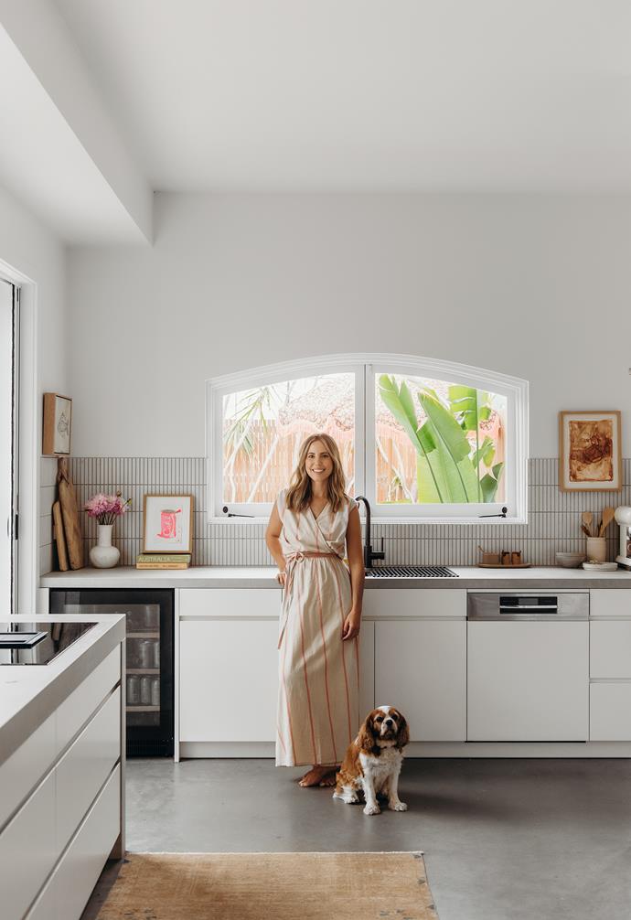 "My husband is the chef so he dictated the appliances," admits Annie (with Max the King Charles cavalier). Urban Joinery built the custom kitchen. "We did a pared-back, lipped-edge cabinetry except for the top row of cabinetry, which is a thin, slatted profile to tie in with the splashback tiles from Academy Tiles," Annie says. The benchtop is Caesarstone Primordia and they chose a polished concrete floor. The artwork on the right is by Loralee Jade.