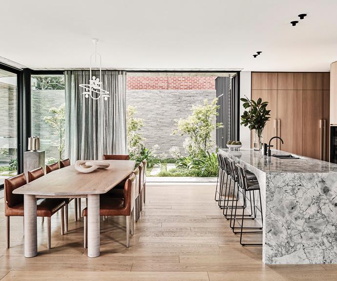The room's centrepiece is the oversized marble [island bench](https://www.homestolove.com.au/15-of-the-best-kitchen-benches-13723|target="_blank") and its striking curve on the dining side. "We saw the stone as an opportunity to continue the grand curvaceous forms that are found within the original architecture, both inside and outside the home," says Berit. The same natural stone was used as a splashback and teamed with cabinetry in a timber-look veneer. "Ultimately, I was after something that was practical and didn't show fingermarks because I didn't want to be cleaning it constantly," says Sarah. To recreate the [indoor/outdoor lifestyle](https://www.homestolove.com.au/12-indoor-outdoor-ideas-for-a-stunning-entertaining-area-18680|target="_blank") that the family enjoyed in Phuket, she says the dining space was designed with receding doors that completely open up the space. "It's perfect for entertaining because everyone can spill out into the garden. The Christmas after we moved in, we had about 24 people in that area." Dining table and chairs, [Jardan](https://www.jardan.com.au/|target="_blank"|rel="nofollow"). Paperclip pendant light, [Anna Charlesworth](https://www.annacharlesworth.com.au/|target="_blank"|rel="nofollow").