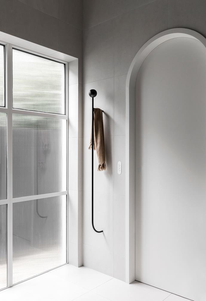Generously sized windows fill the bathroom with natural light. A matte black towel rail from Linear Standard breaks up the sparse expanse of the walls.